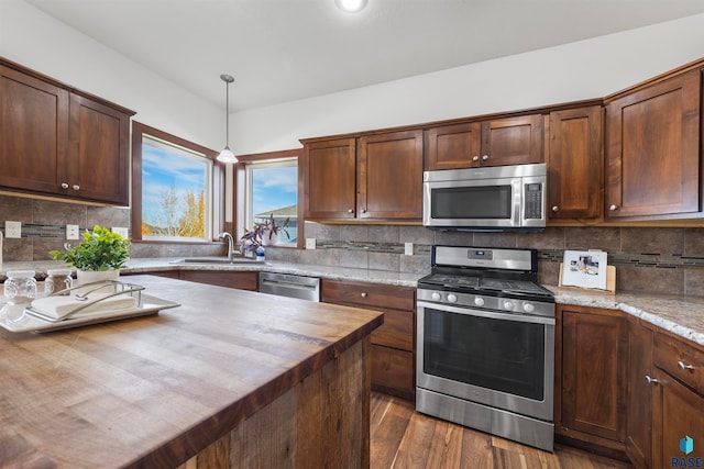 kitchen with sink, appliances with stainless steel finishes, tasteful backsplash, hanging light fixtures, and dark wood-type flooring