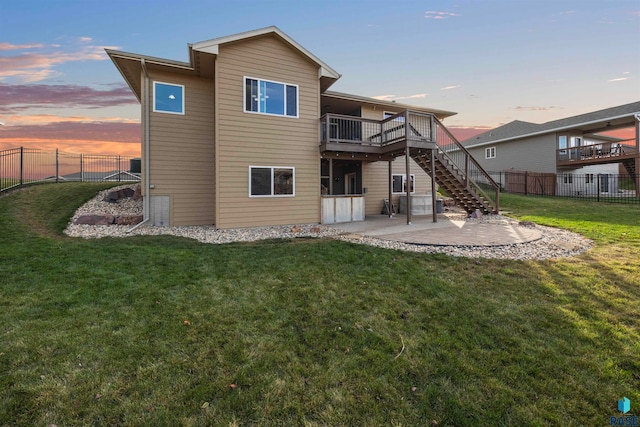 back house at dusk featuring a patio area, a lawn, and a wooden deck