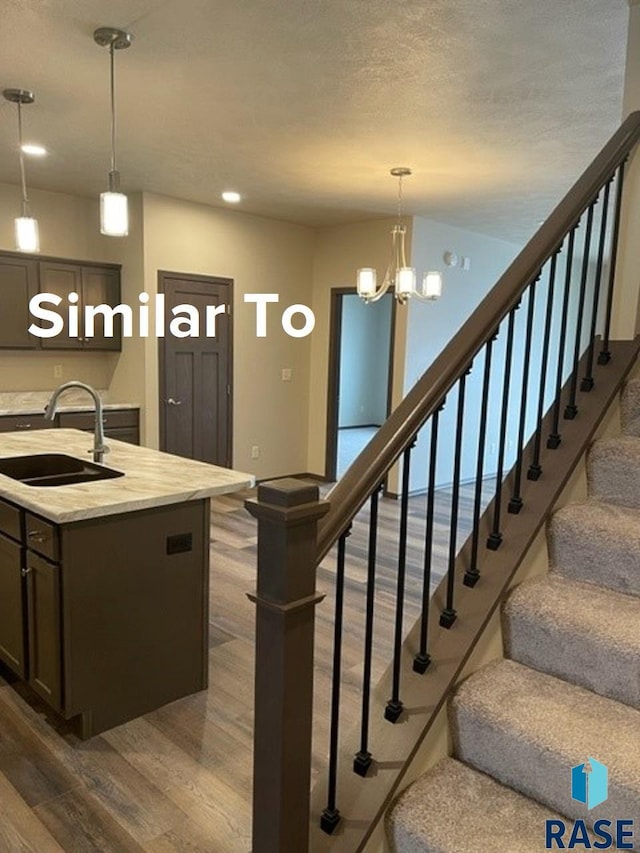 staircase with wood-type flooring, a textured ceiling, sink, and a notable chandelier