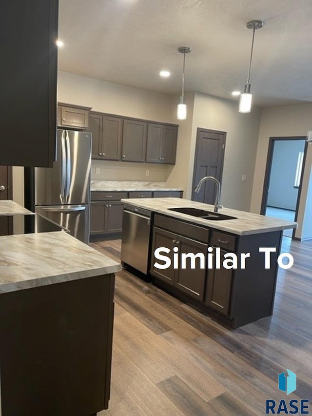 kitchen with stainless steel appliances, a center island with sink, sink, pendant lighting, and light hardwood / wood-style flooring