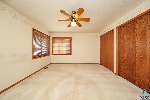 unfurnished bedroom featuring two closets, ceiling fan, light colored carpet, and a textured ceiling