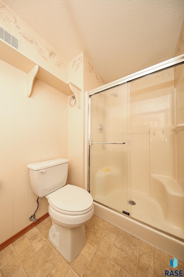 bathroom featuring tile patterned floors, a shower with shower door, a textured ceiling, and toilet