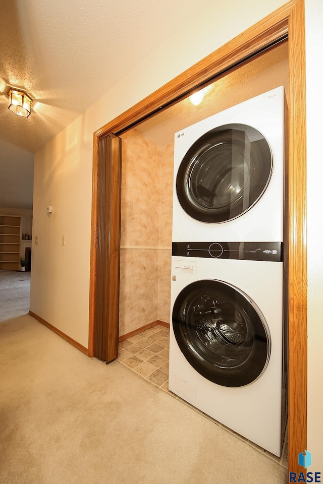 clothes washing area with a textured ceiling, light colored carpet, and stacked washer / drying machine