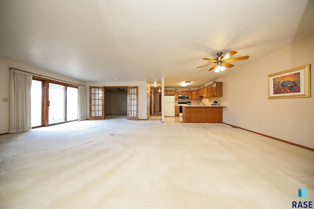 unfurnished living room featuring light carpet, french doors, ceiling fan, and a textured ceiling