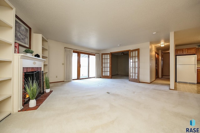 unfurnished living room featuring a fireplace, a textured ceiling, light carpet, and french doors