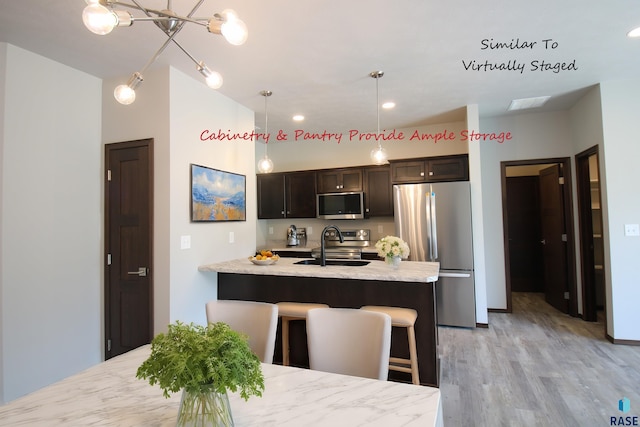 kitchen with appliances with stainless steel finishes, dark brown cabinetry, sink, hanging light fixtures, and a breakfast bar area