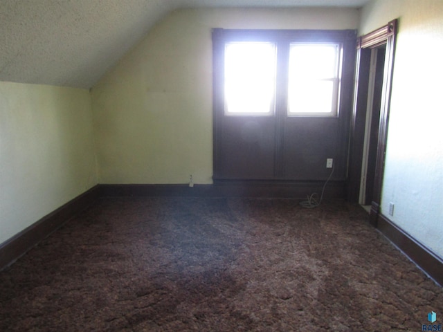 bonus room with a textured ceiling, dark colored carpet, and lofted ceiling