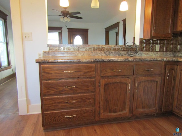 kitchen featuring hardwood / wood-style floors, light stone countertops, decorative backsplash, and ceiling fan