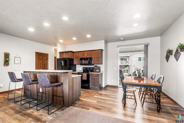 kitchen featuring black appliances, a kitchen breakfast bar, a textured ceiling, light hardwood / wood-style flooring, and a kitchen island