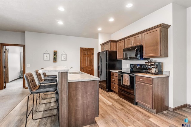 kitchen with black appliances, light wood-type flooring, a kitchen island with sink, and a breakfast bar area