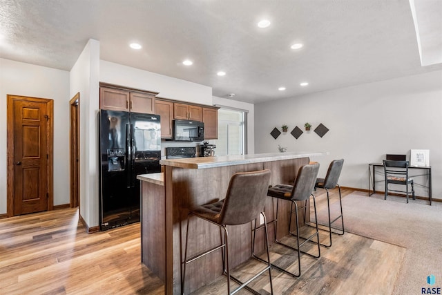 kitchen with light hardwood / wood-style floors, a breakfast bar, black appliances, a textured ceiling, and a center island