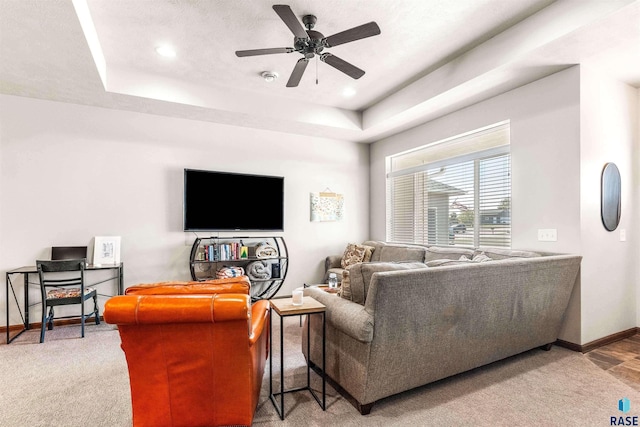 carpeted living room with a textured ceiling, ceiling fan, and a raised ceiling