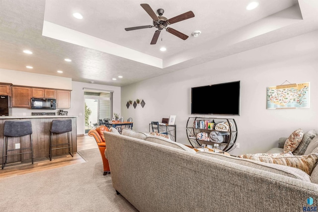 carpeted living room featuring ceiling fan and a raised ceiling