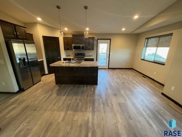 kitchen with a center island with sink, light wood-type flooring, appliances with stainless steel finishes, decorative light fixtures, and lofted ceiling