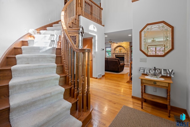 stairs with a brick fireplace, hardwood / wood-style flooring, ceiling fan, and a high ceiling