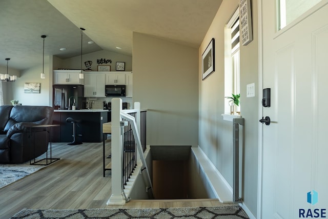 interior space with a kitchen breakfast bar, white cabinets, vaulted ceiling, black appliances, and decorative light fixtures