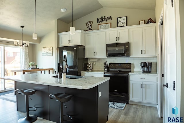 kitchen featuring white cabinetry, pendant lighting, a center island with sink, vaulted ceiling, and black appliances