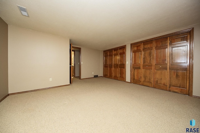 unfurnished bedroom featuring light carpet, a textured ceiling, and multiple closets