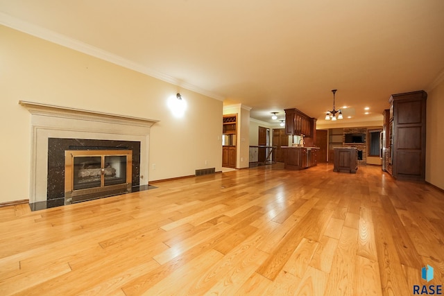 unfurnished living room with light hardwood / wood-style flooring, a chandelier, crown molding, and a fireplace