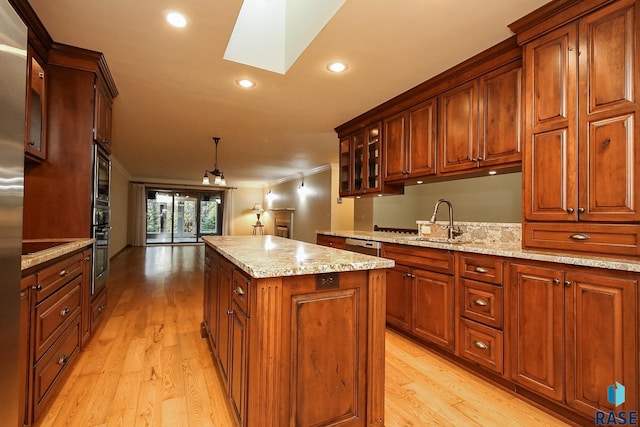 kitchen featuring a skylight, light stone countertops, a center island, light hardwood / wood-style floors, and decorative light fixtures