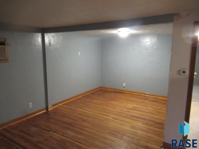 basement featuring wood-type flooring and a wall unit AC