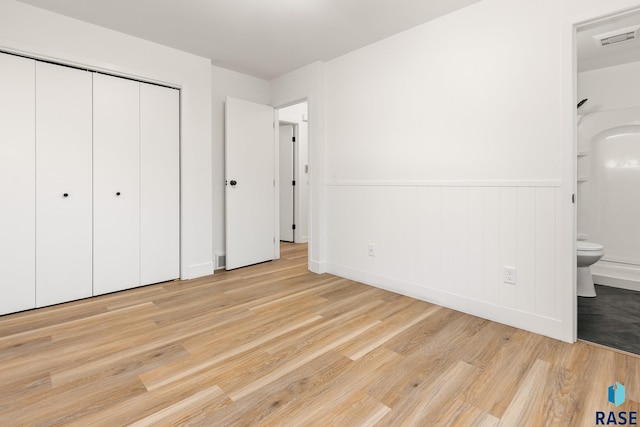 unfurnished bedroom featuring ensuite bathroom, light hardwood / wood-style flooring, and a closet