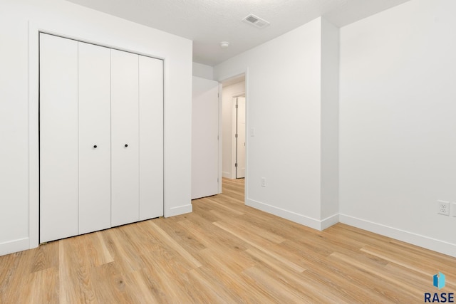 unfurnished bedroom with a textured ceiling, light wood-type flooring, and a closet