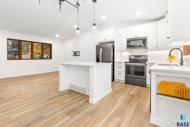 kitchen featuring stainless steel appliances, vaulted ceiling, sink, pendant lighting, and white cabinets