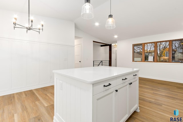 kitchen featuring pendant lighting, vaulted ceiling, light wood-type flooring, a kitchen island, and white cabinetry