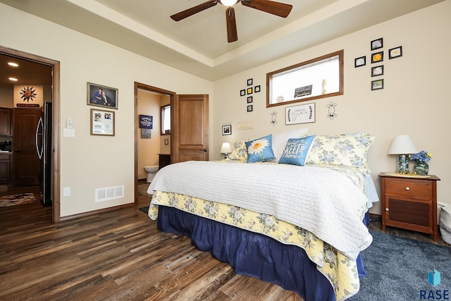 bedroom with ceiling fan, dark wood-type flooring, stainless steel refrigerator, and ensuite bath