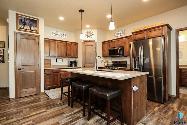 kitchen with appliances with stainless steel finishes, decorative light fixtures, a kitchen island with sink, and dark wood-type flooring