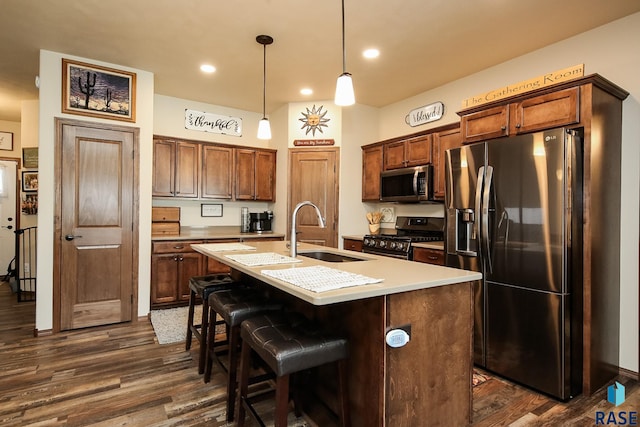 kitchen with sink, dark wood-type flooring, an island with sink, decorative light fixtures, and appliances with stainless steel finishes