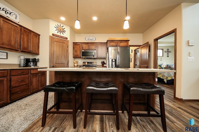 kitchen with a kitchen breakfast bar, dark hardwood / wood-style floors, appliances with stainless steel finishes, decorative light fixtures, and a kitchen island