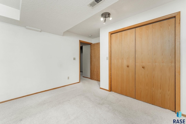 unfurnished bedroom featuring a textured ceiling, light carpet, and a closet