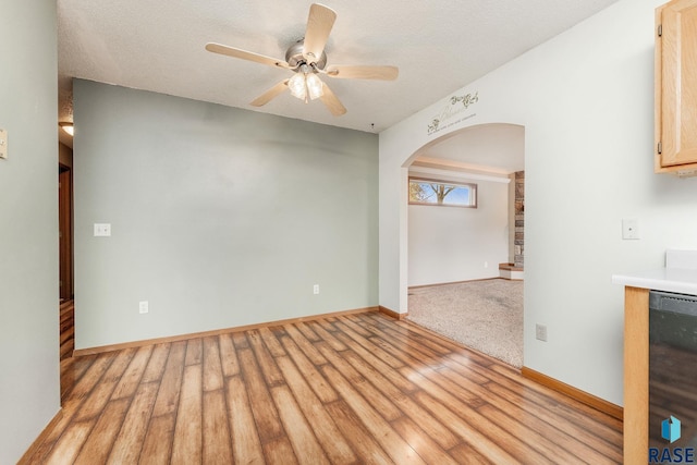 unfurnished room with a textured ceiling, light wood-type flooring, and ceiling fan