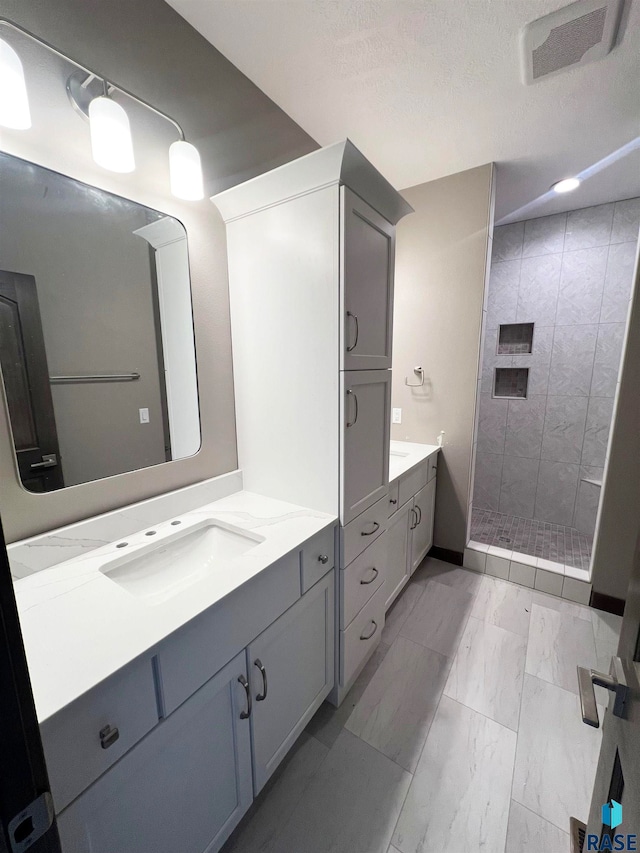 bathroom with vanity, a textured ceiling, and a tile shower