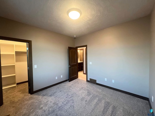 unfurnished bedroom with a walk in closet, a closet, a textured ceiling, and carpet flooring