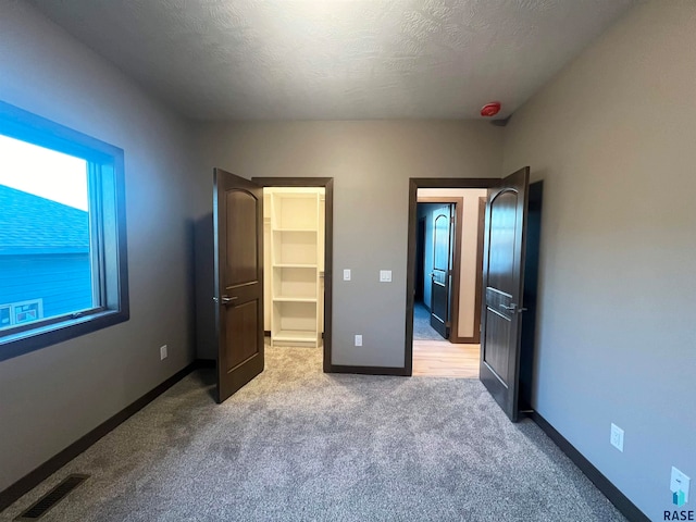 unfurnished bedroom featuring a spacious closet, light carpet, and a textured ceiling