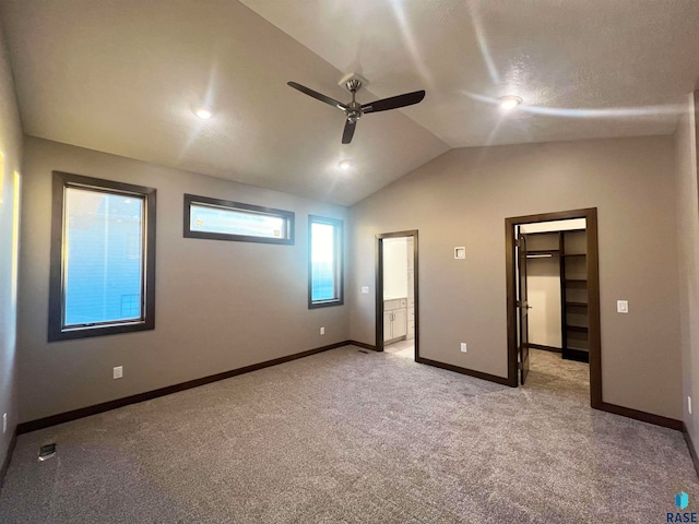 unfurnished bedroom with ensuite bathroom, lofted ceiling, a spacious closet, ceiling fan, and light carpet