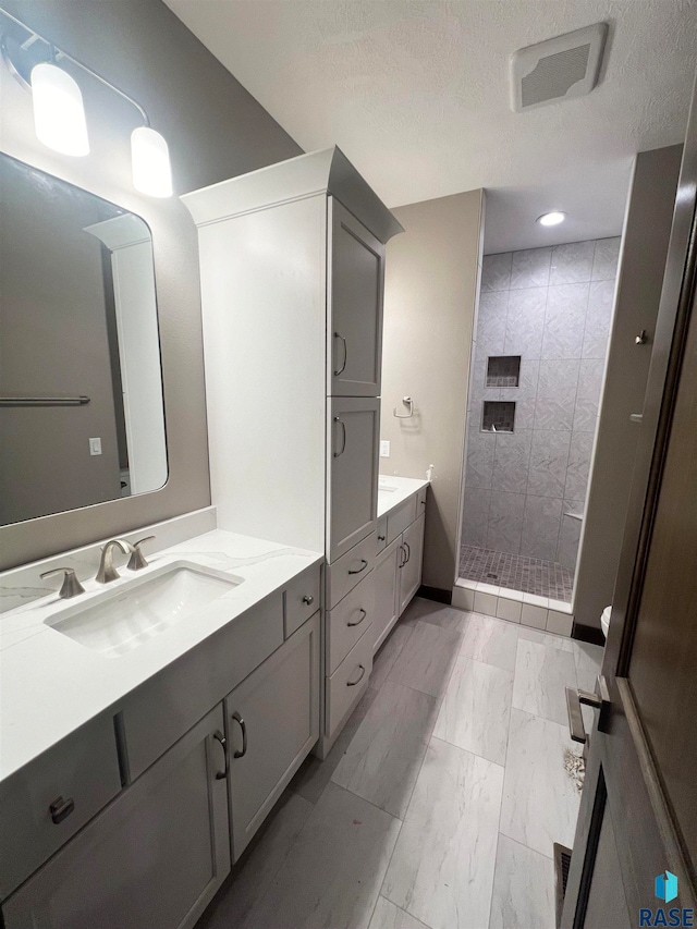 bathroom featuring vanity, a tile shower, and a textured ceiling