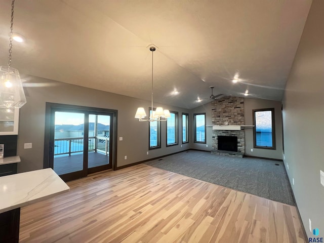 unfurnished living room featuring vaulted ceiling, a wealth of natural light, a fireplace, and light wood-type flooring