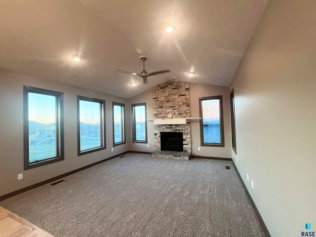 unfurnished living room with ceiling fan, lofted ceiling, a stone fireplace, and carpet floors