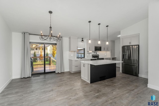 kitchen with light wood-type flooring, appliances with stainless steel finishes, a center island, and decorative light fixtures