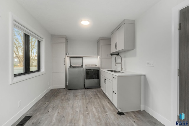 kitchen with independent washer and dryer, sink, and light hardwood / wood-style flooring