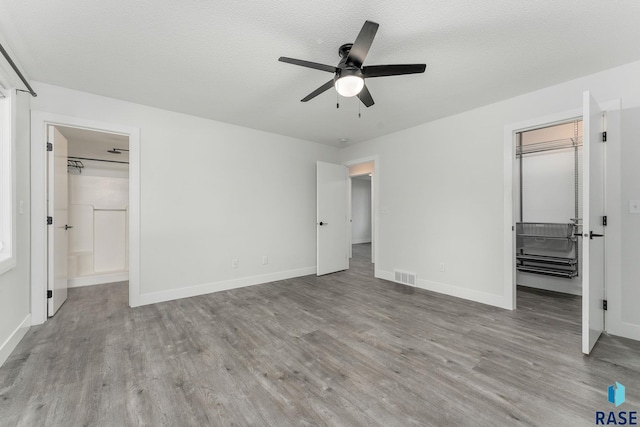 unfurnished bedroom with ensuite bath, ceiling fan, a textured ceiling, a walk in closet, and light wood-type flooring