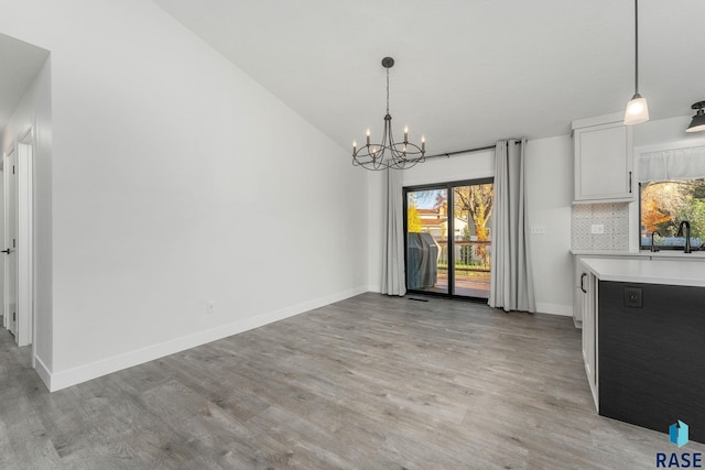 unfurnished dining area with an inviting chandelier, light wood-type flooring, sink, and vaulted ceiling