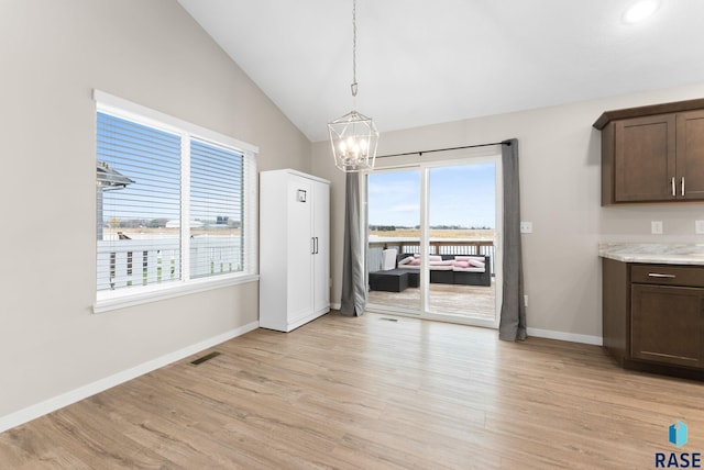 unfurnished dining area with a notable chandelier, plenty of natural light, light wood-type flooring, and vaulted ceiling