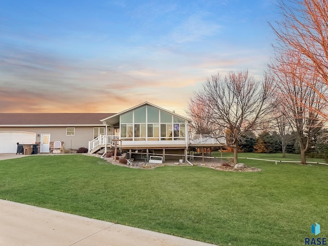 back house at dusk featuring a sunroom, a garage, and a yard