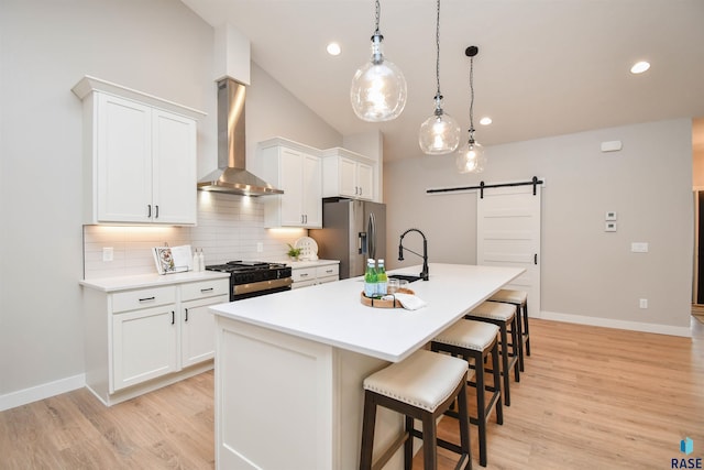 kitchen featuring white cabinets, wall chimney range hood, hanging light fixtures, a barn door, and stainless steel appliances