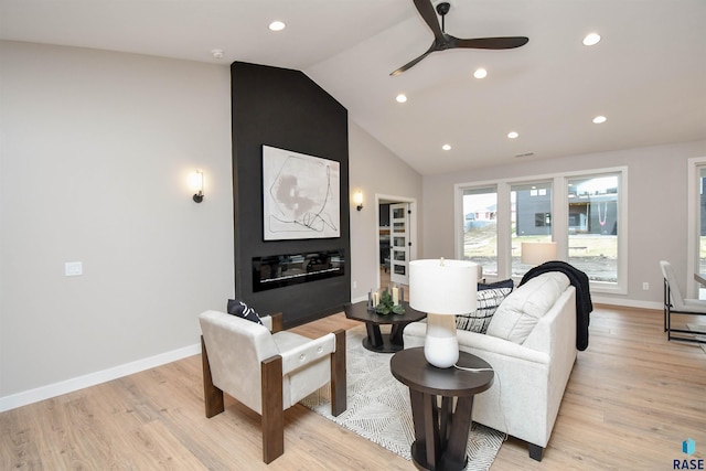 living room featuring ceiling fan, a large fireplace, light wood-type flooring, and vaulted ceiling